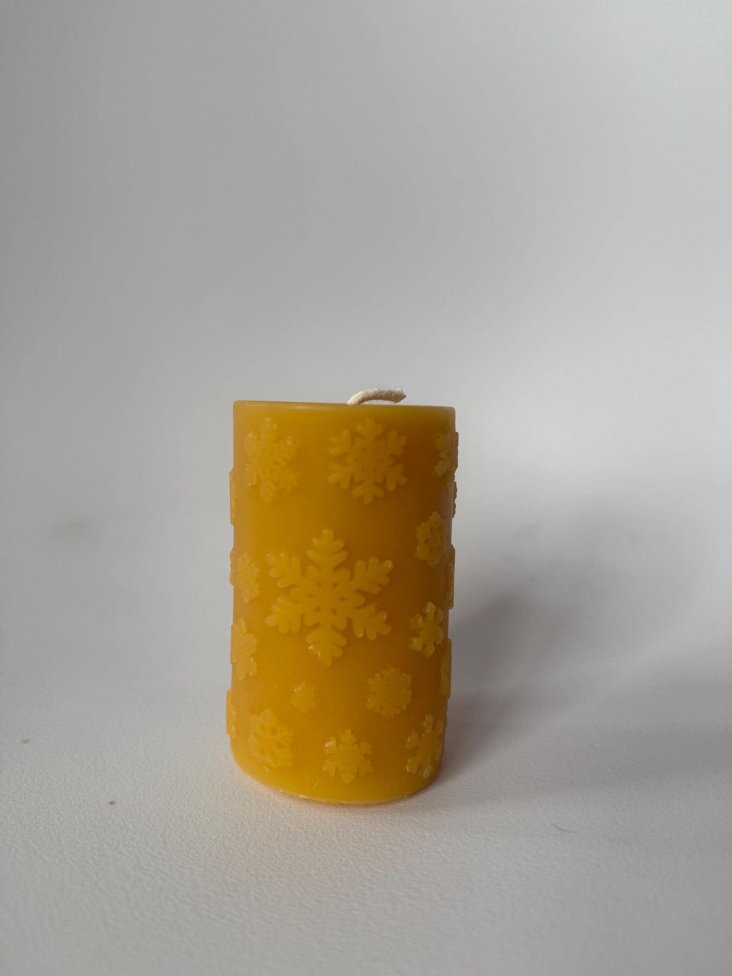 yellow beeswax candle with snowflake pattern on a white background