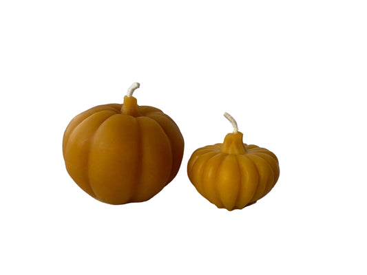 Two pumpkin-shaped beeswax candles on a white surface, one larger than the other