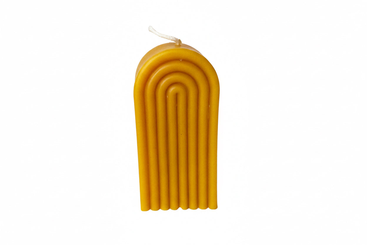 yellow beeswax candle with a ribbed design on a white surface, looks like a rainbow