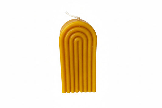 yellow beeswax candle with a ribbed design on a white surface, looks like a rainbow