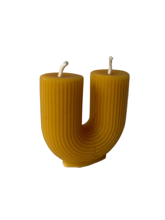 beeswax candle shaped like the letter 'U' on a gray background